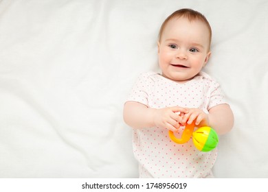 Cute Baby Girl Playing With Rattle On Bed. Top View