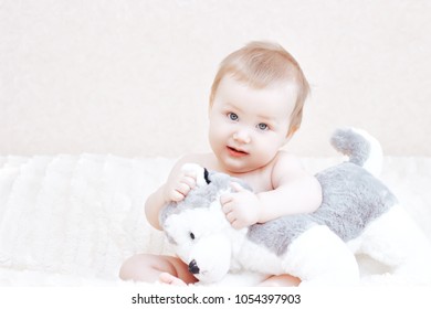 Cute baby girl playing with soft toy on bed in bedroom