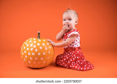 Cute baby girl with polka dots pumpkin on the orange background. haloween concept.
