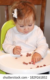 Cute baby girl sitting in her high chair self feeding solid foods baby led weaning