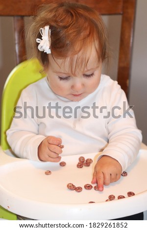 Cute baby girl sitting in her high chair self feeding solid foods baby led weaning