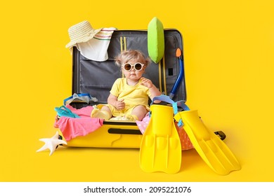 Cute Baby Girl In Suitcase With Belongings On Color Background