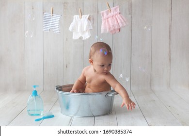Cute baby girl takes a bath. Basin on wooden backgroun. Clothes are dried on a hanger.