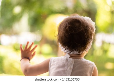 Cute Baby Girl In A White Gown Leaning On A Window Glass And Looking Outside On A Green Park, While Waiting For Her Parents To Come Back To Home.