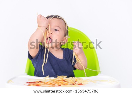 Cute baby happy to play and having fun eating spaghetti in high chair.The concept of baby development learning to eat and handling.