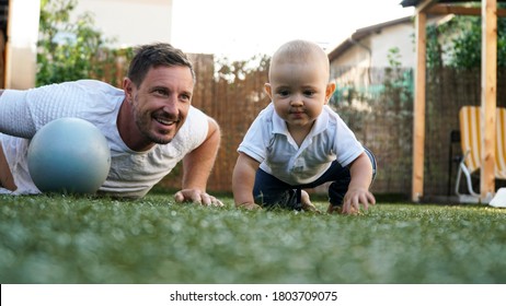 A cute baby and his smiling father playing on a grass with a ball