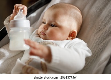 Cute Baby Laying In Bouncer Chair With Milk Bottle. Child Relaxing In Swing. Adorable Newborn Baby In Bodysuit In Sunny Bedroom. Family Morning At Home. Selective Focus. Alternative To Breast Feeding.