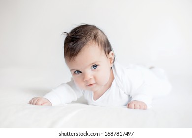 cute baby lies on stomach in bed on a white blanket look into camera. Two months kid development of child up to a year. Sweet and light childhood care and parenthood concept
