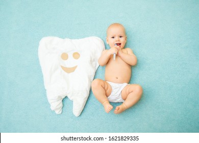 Cute baby lies with a toothbrush on a blue background. White tooth made of fabric. Medicine, dentistry, health concept
