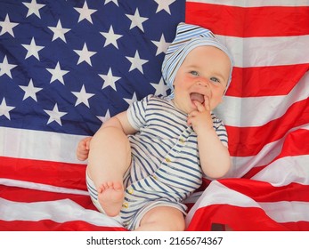 A Cute Baby Is Lying On The American Flag. A Happy Infant Plays Swinging On A Swing Against The Background Of The National Flag Of The United States Of America.