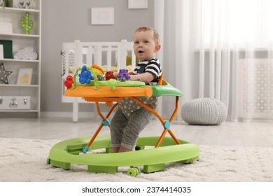 Cute baby making first steps with toy walker at home, space for text