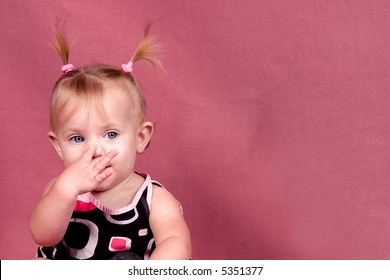 A Cute Baby On A Pink Background Touching Her Nose