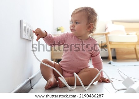 Cute baby playing with electrical socket and plug at home. Dangerous situation