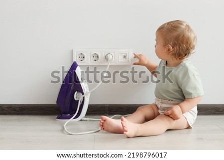 Cute baby playing with electrical socket and iron plug at home. Dangerous situation