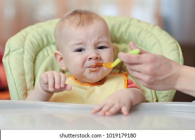 Cute baby refusing to eat food from spoon with face dirty of vegetable puree.