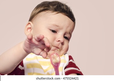 Cute baby refusing to eat baby food from the spoon. Six month old beginning food diversification. Little child cringing and pushing the spoon with food.