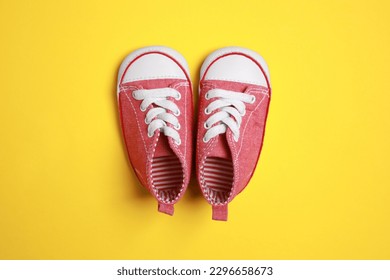 Cute baby shoes on yellow background, flat lay