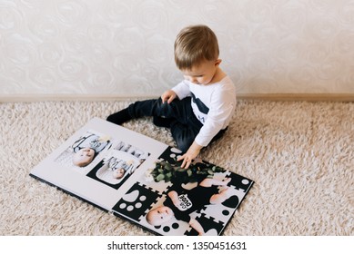 Cute Baby Sitting And Looking At A Large Stylish Photo Book With Their Photos. Children's Photo Album