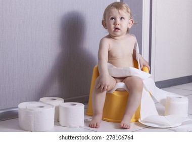 Cute baby sitting on chamber pot with toilet paper rolls