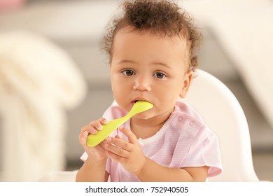Cute baby with spoon sitting in room