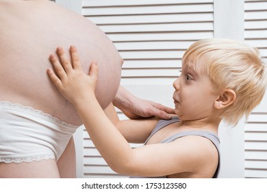 Cute Baby Stares Into Belly Of Pregnant Mother. Second Pregnancy Concept.