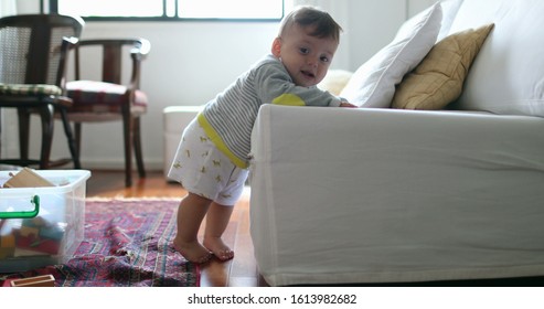 
Cute Baby Toddler Leaning On Sofa Learning To Stand Up. Adorable Infant Child Learning To Stand Holding Into Couch