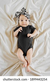 Cute Baby In Trendy Garment And Leopard Headband And Black Bodysuit  Lying On Bed. Stylish  Infant In Trendy Outfit. Fashion Baby Girl