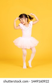 Cute Ballerina Little Asian Girl In Pink Dancer Over A Yellow Background. Kid In Dance Class. Child Girl Is Studying Ballet.