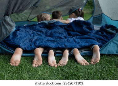 cute bare feet of three children peeking out of sleeping bag. Children, brothers and sisters or friends lie on their stomachs in tent. Healthy lifestyle, little tourist, family activities, summer fun - Powered by Shutterstock