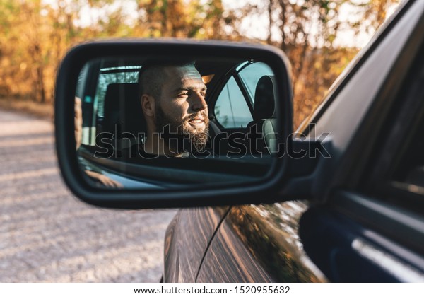 Cute, bearded guy driving a\
car, reflection in car rearview mirror. Transportation, urban\
concept