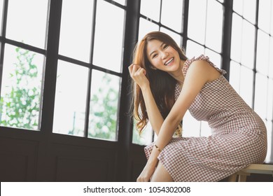 Cute and beautiful Asian girl smiling in coffee shop or modern office, copy space on windows. Happy young people, college university student, modern lifestyle, or women fashion advertisement concept