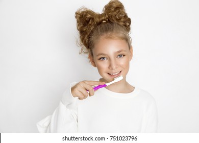 Cute, beautiful blonde, young girl holding a toothbrush and smiling happily. The girl is washing her teeth.