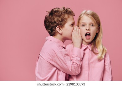 cute, beautiful children are standing in pink clothes on a pink background and the boy tells the girl secrets in her ear. Topics of friendship and relationships - Shutterstock ID 2198103593