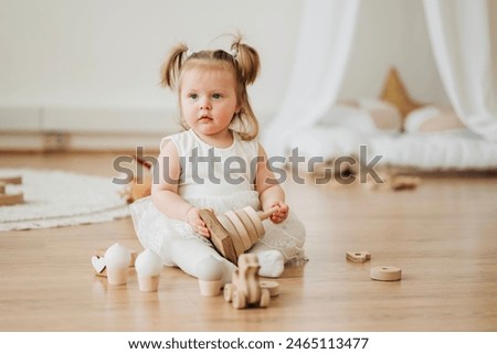 Cute beautiful girl baby sitting on the floor in the children's room and playing in eco wooden toys cubes and pyramid