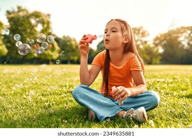 Cute beautiful girl blowing soap bubbles sitting on the grass in the meadow in the park, playing and having fun on a warm sunny weekend. - Powered by Shutterstock