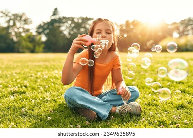 Cute beautiful girl blowing soap bubbles sitting on the grass in the meadow in the park, playing and having fun on a warm sunny weekend. - Powered by Shutterstock