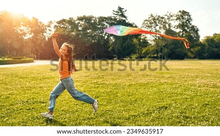 Cute beautiful little girl running and playing with a colorful kite in a meadow in a park on a warm sunny weekend.