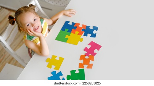 A cute beautiful little innocent girl is sitting at a table with large colorful puzzles. A puzzle for preschool development. The symbol of autism - Powered by Shutterstock