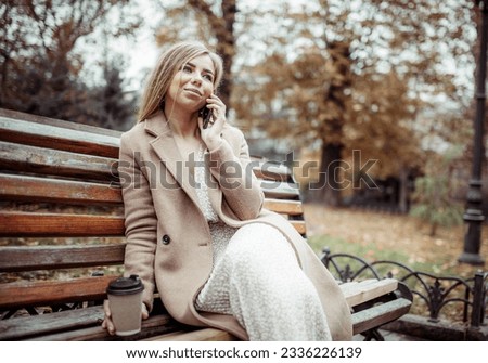 Cute beautiful woman talking on the phone while sitting on a bench in the autumn park