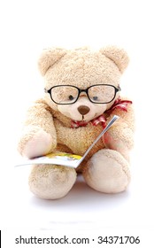 A cute beige teddy bear for kids to play with wearing eyeglasses, holding and reading a little book. Image isolated on white studio background.