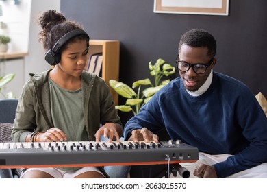 Cute biracial girl in headphones repeating after her music teacher touching keys of piano keyboard - Powered by Shutterstock