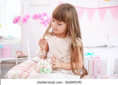 Cute birthday girl eating sweets while sitting on bed at home