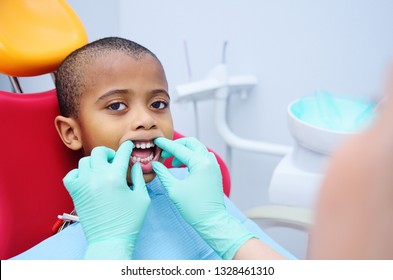Cute Black Baby Boy African American Smiling Sitting In The Dental Chair At The Examination At The Children's Dentist.