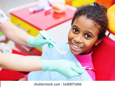 Cute Black Baby Girl Smiling Sitting In A Red Dental Chair At The Examination At The Children's Dentist