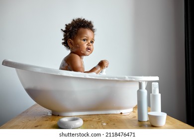 cute black baby girl takes bath. in white Bathroom. girl bathes in basin alone, at home, in the morning at weekends. Happy healthy boy or girl playing, splashing and having fun during bathtime.