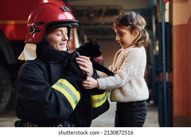 Cute black cat. Happy little girl is with female firefighter in protective uniform.