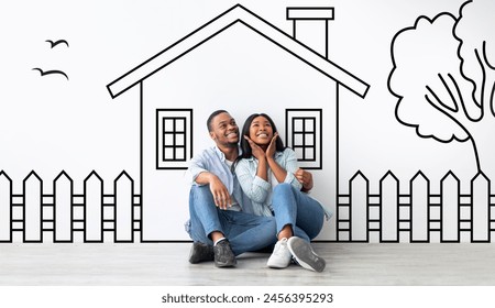 Cute black family husband and wife sitting over drawn on white wall house, embracing and smiling. Real estate, mortgage concept - Powered by Shutterstock