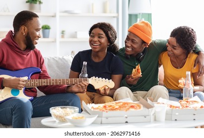 Cute Black Friends Playing Guitar And Singing Songs While Having Party At Home, Sitting On Couch In Living Room, Drinking Beer, Eating Pizza, Joyful African American People Relaxing At Weekend