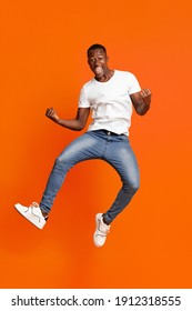 Cute black guy winner jumping up in the air and showing funny figures, having good day, showing positive emotions over orange background. African american man posing at studio, having fun