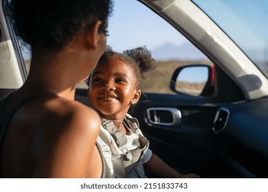 Cute black little girl looking her mother while sitting in car. Cheerful mother and daughter sitting in car during road trip. Smiling and carefree female child laughing with african american mother. - Shutterstock ID 2151833743